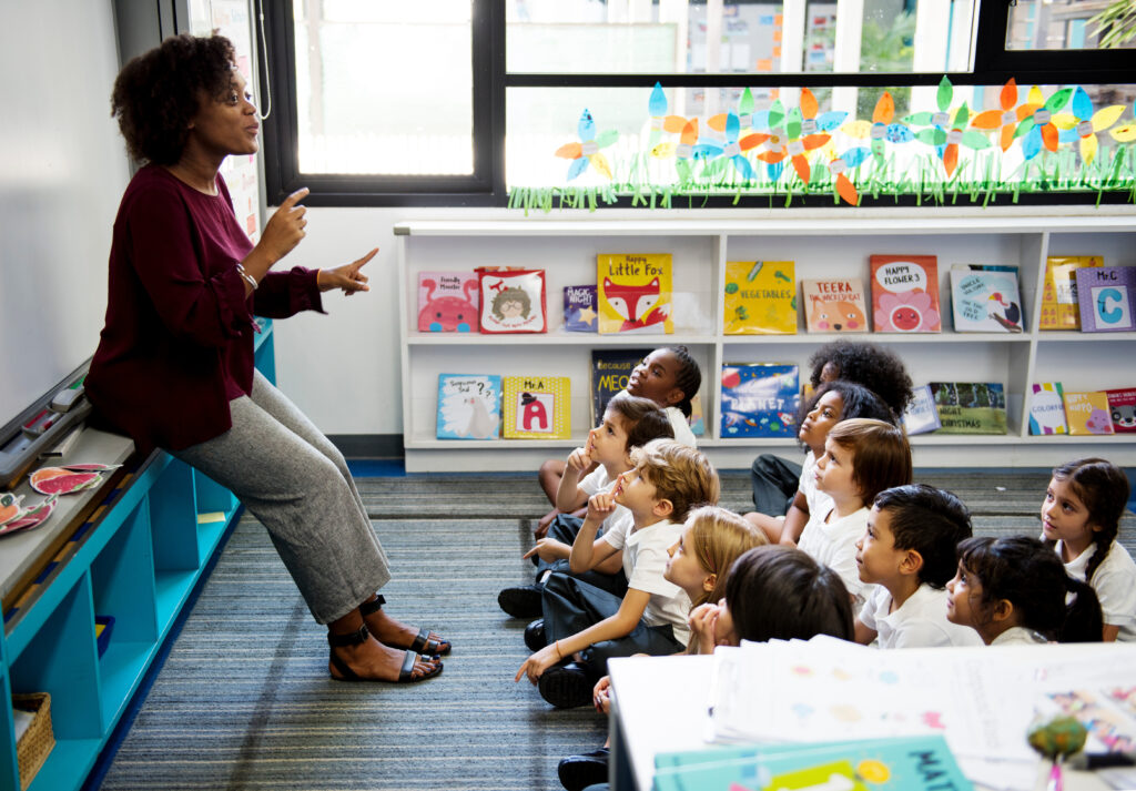 A kindergarten teacher talks to students that sit on the floor