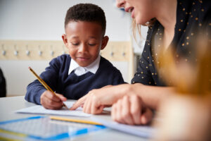 Teacher and student sit at a table and discuss mathematics problem.