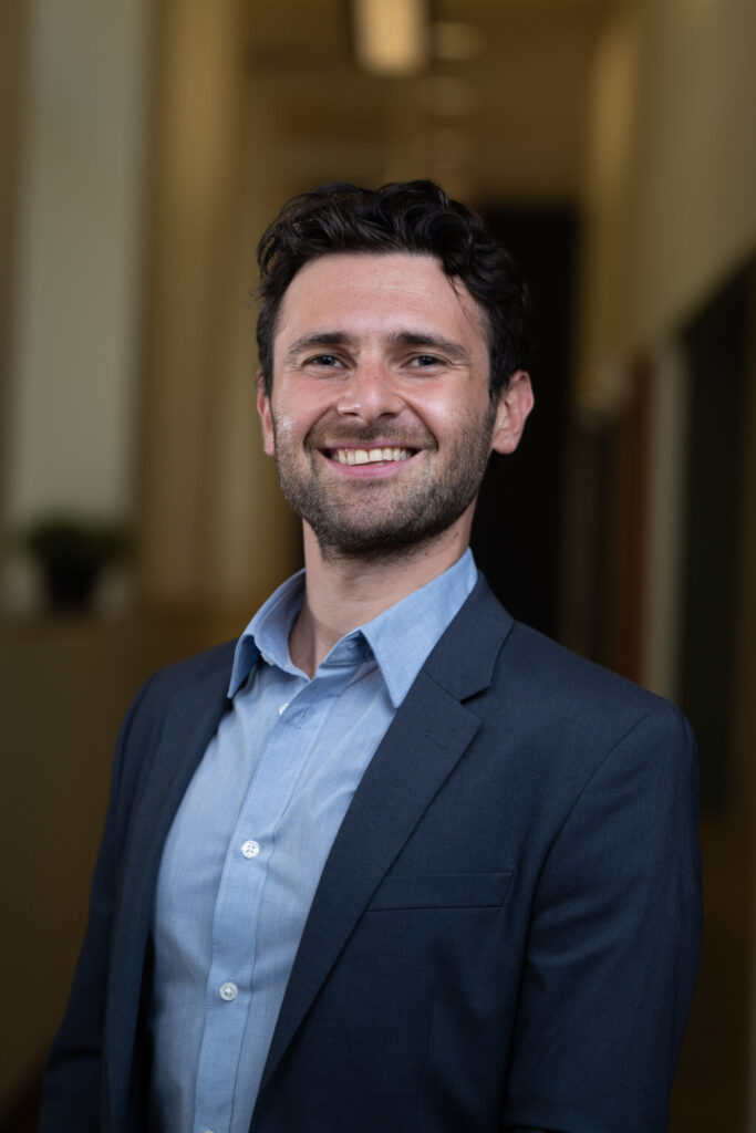 Picture of a man with short brown hair in a blue button-up shirt and a blue suit jacket