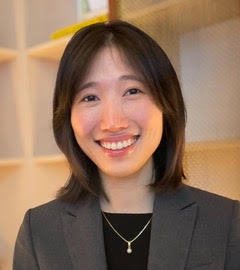 Picture of a Korean woman with shoulder length, dark hair wearing a black shirt and gray suit jacket